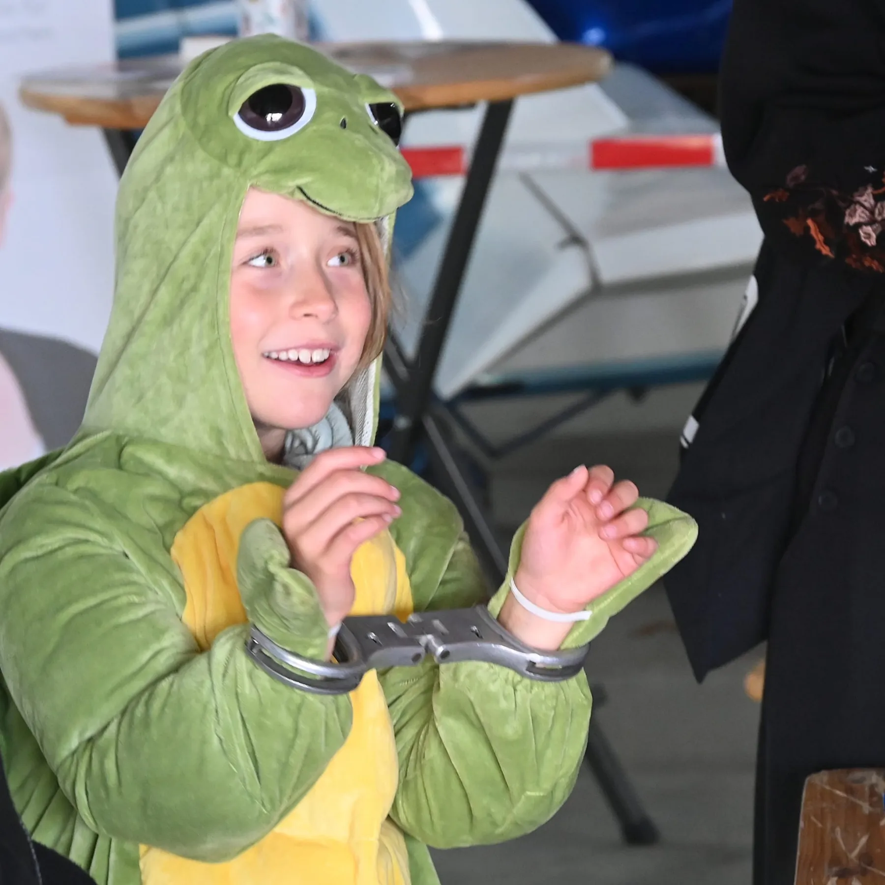 Ein Junge im Froschkostüm zeigt stolz seine Spielzeug-Handschellen.