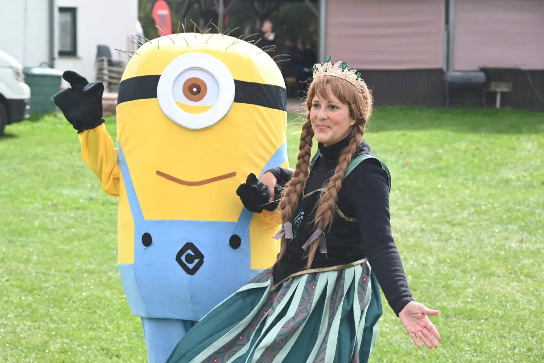Minion und Eiskönigin winken gemeinsam auf der Wiese.
