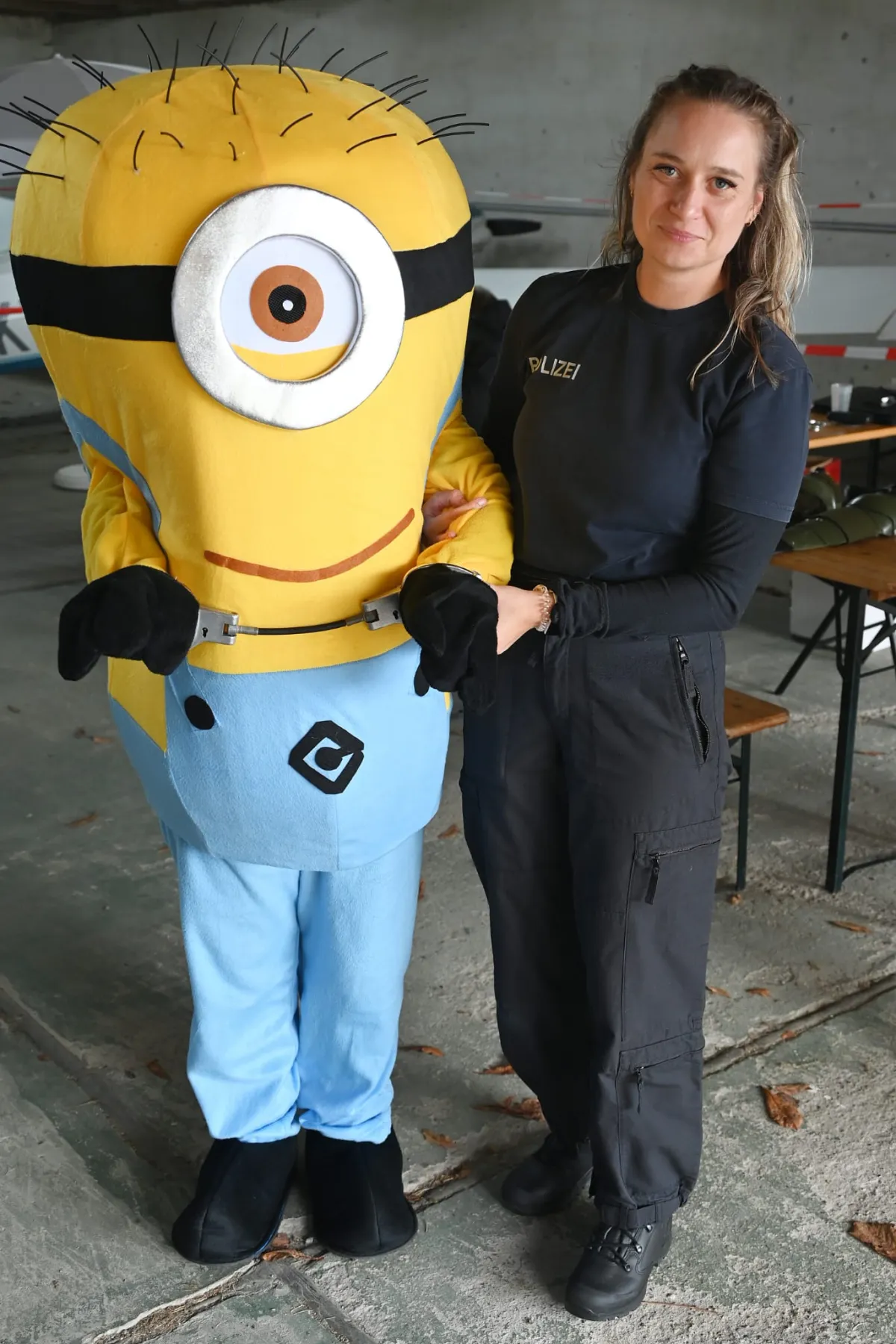 Ein Minion und eine Polizistin stehen Seite an Seite im Hangar.
