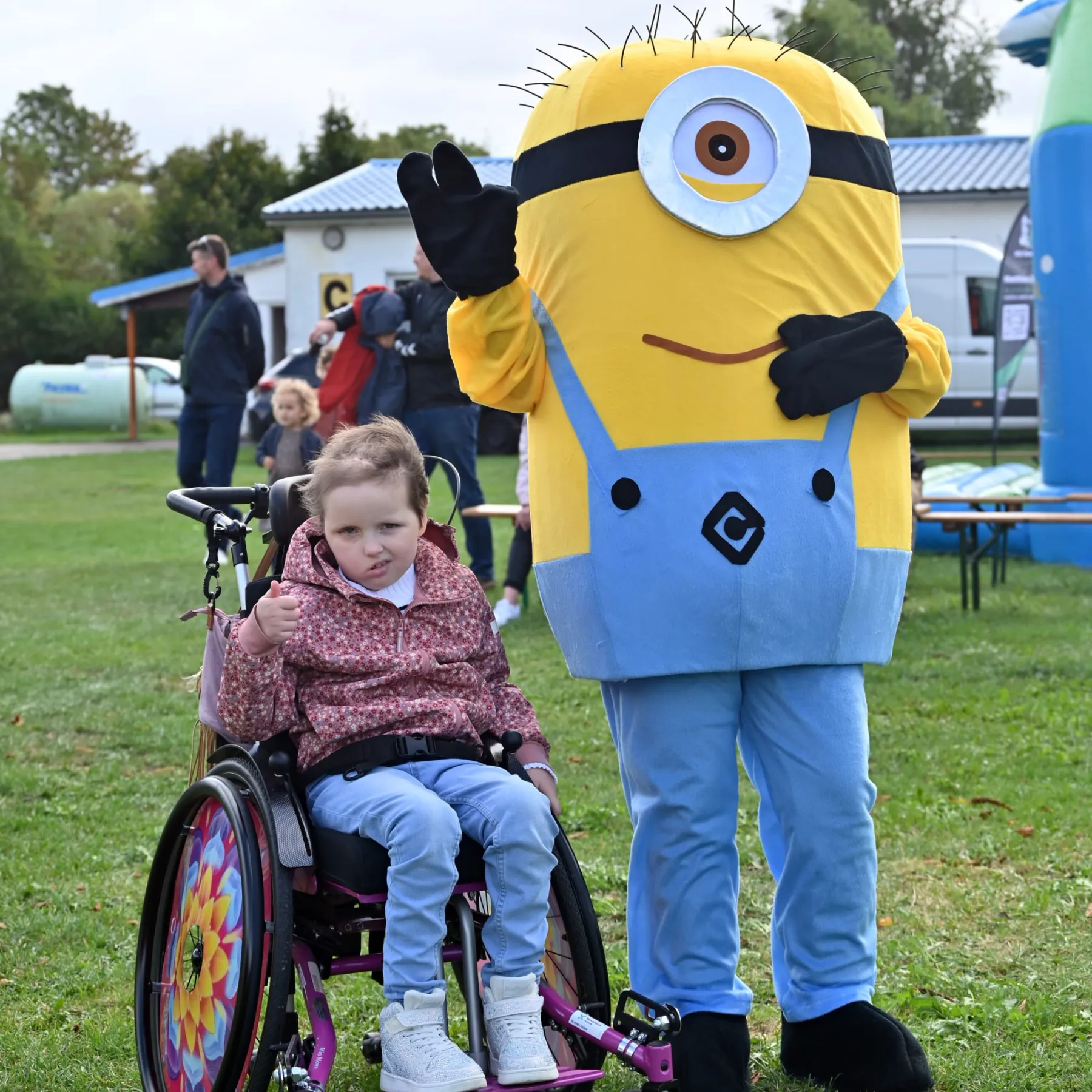 Ein Mädchen im Rollstuhl posiert mit einem Minion auf der Wiese.